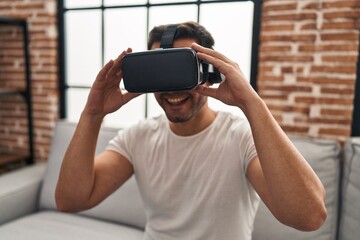 Young hispanic man playing video game using virtual reality glasses at home