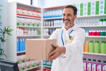 Middle age man pharmacist smiling confident holding package at pharmacy