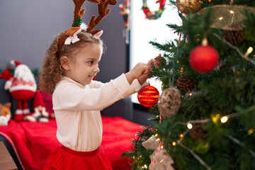 Adorable blonde girl wearing reindeer ears decorating christmas tree at home