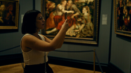 Young beautiful hispanic woman visiting art gallery taking pictures with smartphone at Art Museum in Vienna