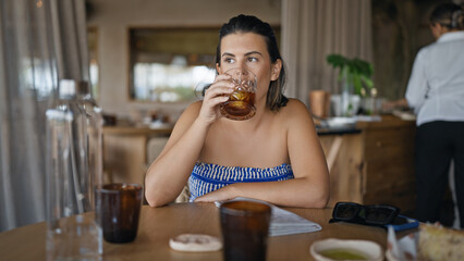Young hispanic woman drinking a glass of vermouth at the restaurant