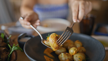 Young hispanic woman eating potatoes at the restaurant