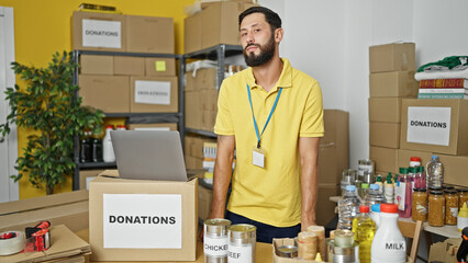 Young hispanic man volunteer standing with serious face at charity center