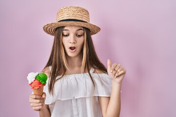 Teenager girl holding ice cream pointing down with fingers showing advertisement, surprised face and open mouth