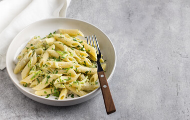 Penne pasta with zucchini, cream cheese and herbs on a gray textured background, top view. Vegetarian food, homemade healthy food