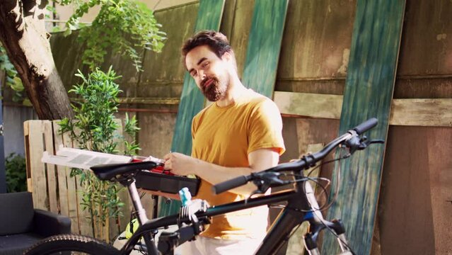 Portrait view of sports-loving male cyclist grasping his bicycle toolkit and looking for specialized tool for repairing in home yard. Caucasian man outdoor gripping toolbox. Dolly zoom-in.