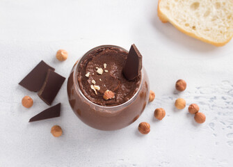 Vegan chocolate paste with banana and nuts surrounded by ingredients: chocolate and hazelnuts on a light gray background