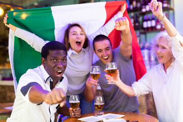 Diverse group celebrating with Italian flag at a pub with beer