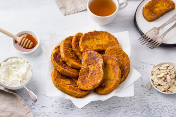 Sweet pumpkin toast with honey and cream, sprinkled with powdered sugar and almond petals on a light blue textured background. Delicious homemade breakfast