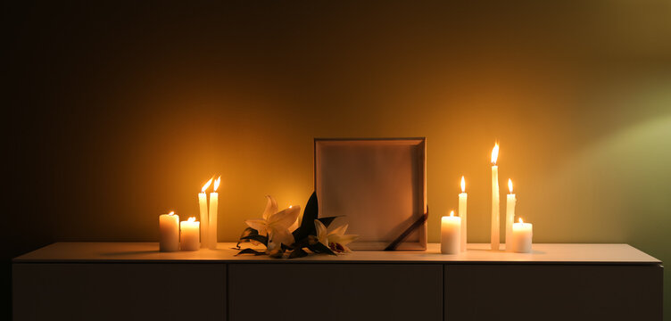 Blank photo frame, glowing candles and lily flowers on table in dark room