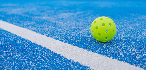 Fototapeta na wymiar banner of a pickleball ball close to the line of a blue pickleball court