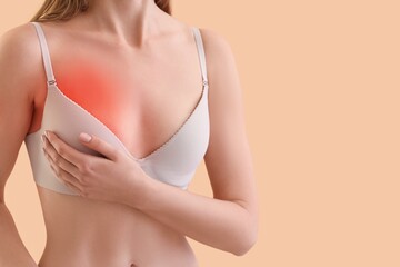 Young woman feeling pain in breast on beige background, closeup. Breast cancer awareness concept