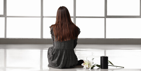 Woman with mortuary urn and lily flowers sitting in empty room, back view