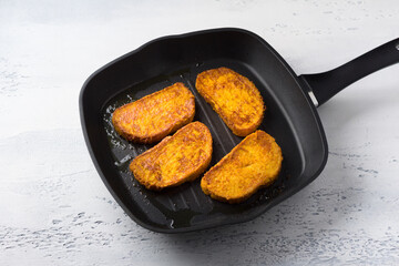 Sweet fried pumpkin toasts with ginger and cinnamon in a frying pan on a light blue table, top view. Cooking stage