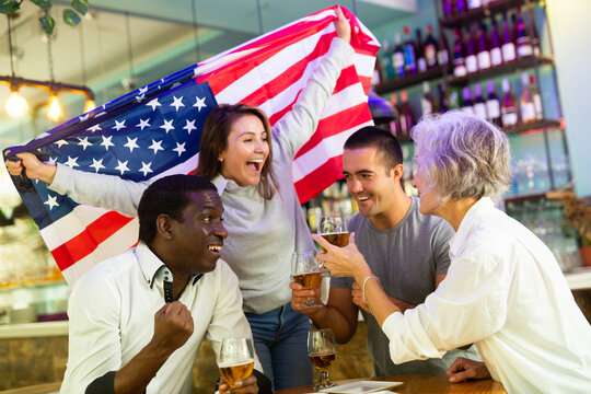 Emotional multiracial american spots supporters with flag of USA happy about victory in championship in pub