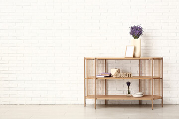 Vase with beautiful lavender flowers and decor on shelving unit near light brick wall in room