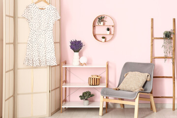 Interior of stylish room with folding screen, shelving unit, chair, ladder, beautiful lavender flowers and shelf hanging on pink wall