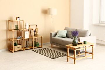 Interior of stylish living room with shelving unit, sofa, lamp, table and beautiful lavender flowers