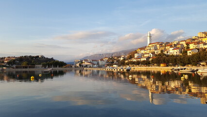 A tranquil lake reflects the sun's golden rays, surrounded by lush greenery and homes on a distant hillside in Croatia