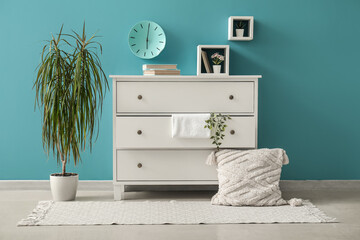 Chest of drawers with decor and houseplant near color wall