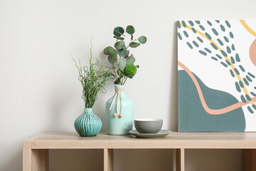 Vases with green plants on wooden cabinet near white wall