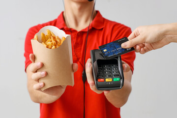 Male worker with french fries taking payment on light background, closeup