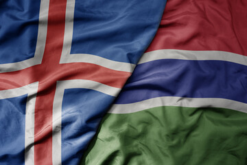big waving national colorful flag of icelandic and national flag of gambia .