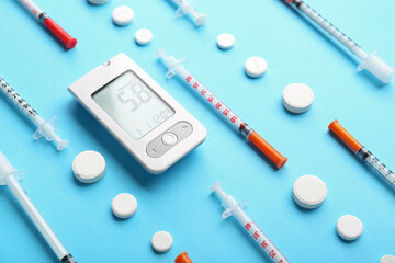 Glucometer with pills and syringes on blue background, closeup. Diabetes concept