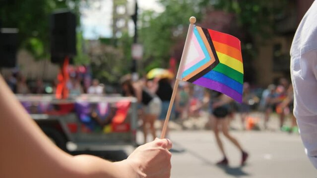 Hand hold Pride Flag and people at pride parade. Close up shot