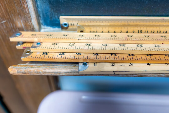 Group of wooden yard sticks and meter sticks with blue background.	