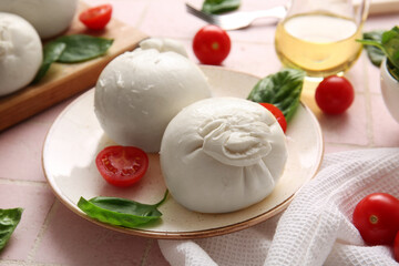 Plate of tasty Burrata cheese with basil and tomatoes on pink tile background