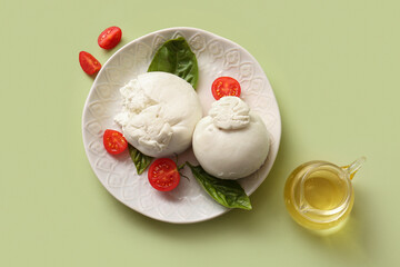 Plate of tasty Burrata cheese with basil and tomatoes on green background