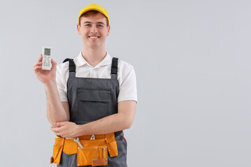 Male technician with air conditioner remote control on light background