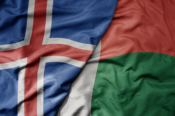 big waving national colorful flag of icelandic and national flag of madagascar .