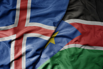 big waving national colorful flag of icelandic and national flag of south sudan .