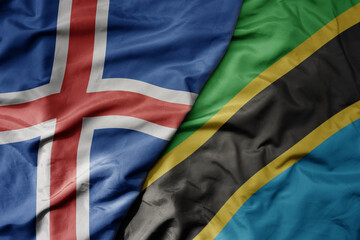 big waving national colorful flag of icelandic and national flag of tanzania .