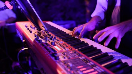 Closeup of piano player's hands slow motion playing keyboard. Red and purple lighting, live music performance