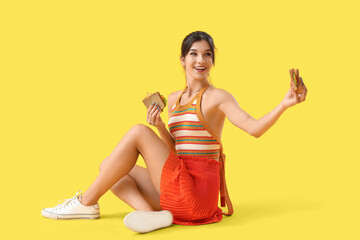 Young woman with tasty sandwiches sitting on yellow background