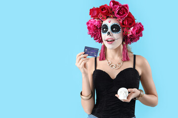 Young woman with painted skull and credit card on blue background. Mexico's Day of the Dead (El Dia de Muertos) celebration
