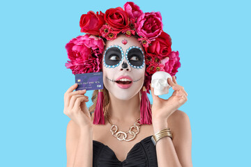 Young woman with painted skull and credit card on blue background. Mexico's Day of the Dead (El Dia...