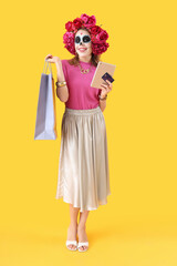 Young woman with tablet computer, credit card and shopping bag on yellow background. Mexico's Day of the Dead (El Dia de Muertos) celebration