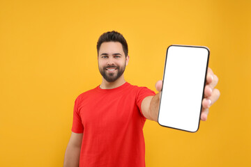 Young man showing smartphone in hand on yellow background