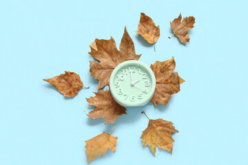 Alarm clock with fallen leaves on blue background