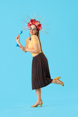 Young Mexican woman with maracas on blue background