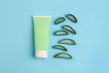 Tube of toothpaste and fresh cut aloe on light blue background, flat lay