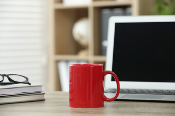 Red ceramic mug, notebooks and laptop on wooden table indoors