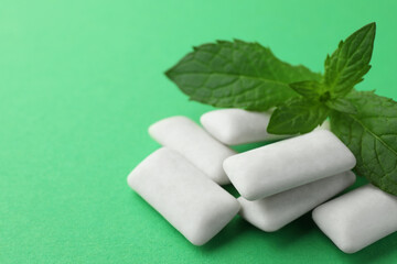 Tasty white chewing gums and mint leaves on green background, closeup. Space for text