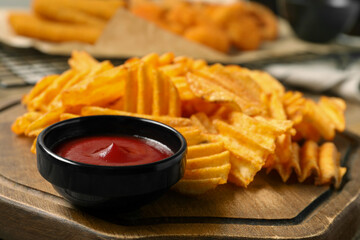 Tasty ketchup and ridged chips on wooden board, closeup