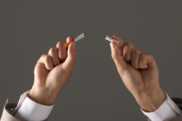 Stop smoking concept. Man holding pieces of broken cigarette on gray background, closeup