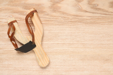Slingshot with leather pouch on wooden background, top view. Space for text
